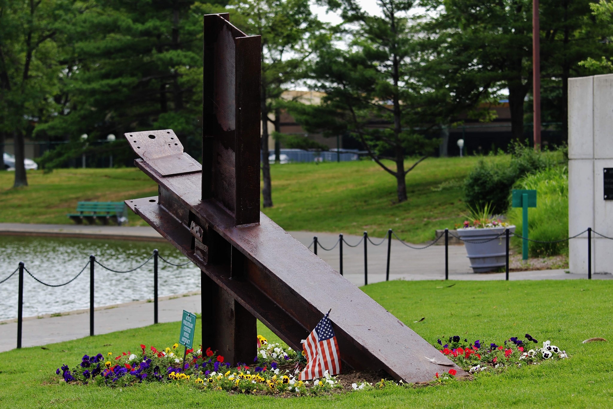 Recovered World Trade Center steel surrounded by flowers beside the water.